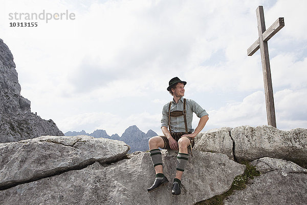 Deutschland  Bayern  Osterfelderkopf  Mann in traditioneller Kleidung am Gipfelkreuz sitzend