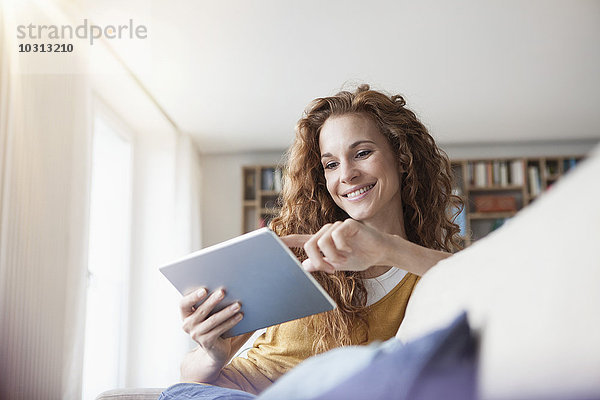 Lächelnde Frau zu Hause auf der Couch sitzend mit digitalem Tablett