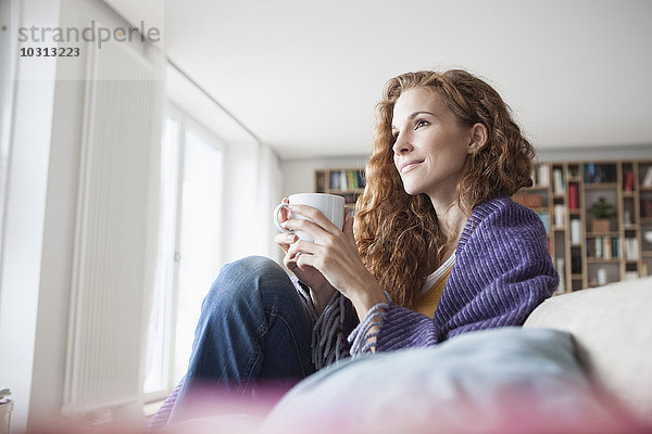 Frau zu Hause auf der Couch sitzend  Tasse haltend