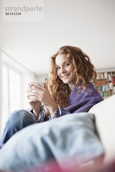 Lächelnde Frau zu Hause auf der Couch sitzend  Tasse haltend