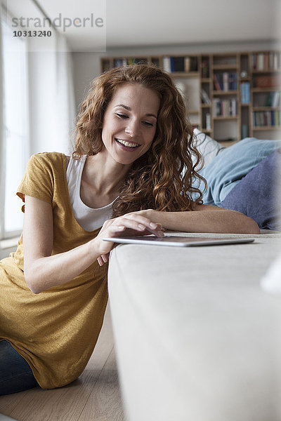 Lächelnde Frau zu Hause mit digitalem Tablett auf der Couch