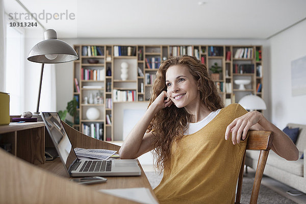 Lächelnde Frau zu Hause mit Laptop auf dem Sekretärinnenschreibtisch