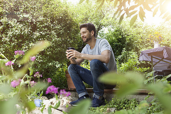 Lächelnder Mann im Garten sitzend mit einer Tasse Kaffee