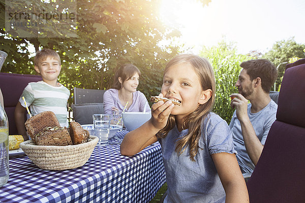 Mädchen beim Brotessen mit der Familie am Gartentisch