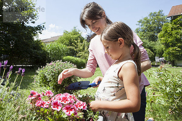 Lächelnde Mutter und Tochter im Garten beim Pflanzen von Blumen