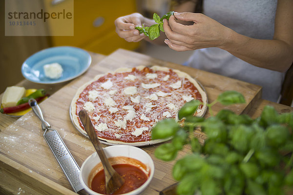 Junge Frau bereitet Pizza mit Mozzarella  Chilischoten und Basilikum zu.