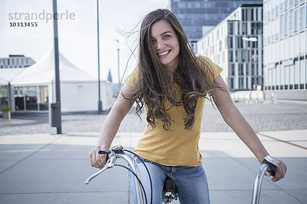 Deutschland  Köln  Porträt einer lächelnden jungen Frau mit blasenden Haaren auf dem Fahrrad