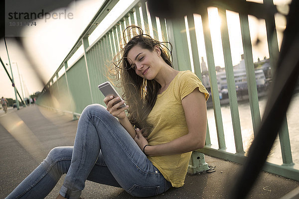 Deutschland  Köln  Frau auf der Rheinbrücke mit Blick auf ihr Smartphone
