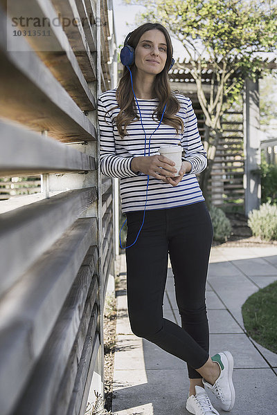 Porträt einer lächelnden Frau mit Kaffee zum Hören von Musik über Kopfhörer
