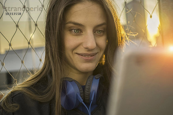 Porträt einer erstaunten jungen Frau  die ihr Smartphone im Gegenlicht betrachtet.