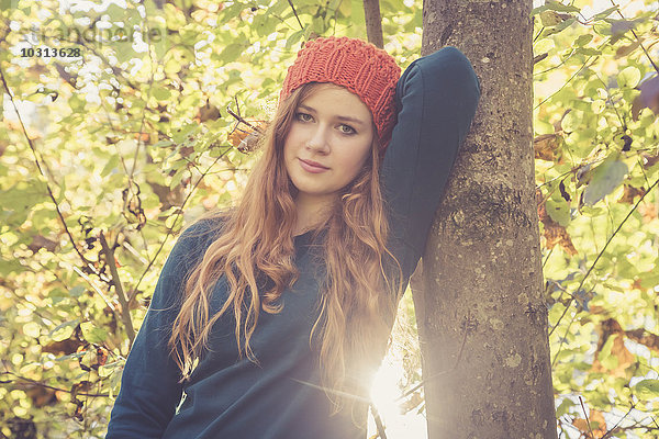 Porträt eines jungen Mädchens  das sich im Herbst an einen Baum lehnt.