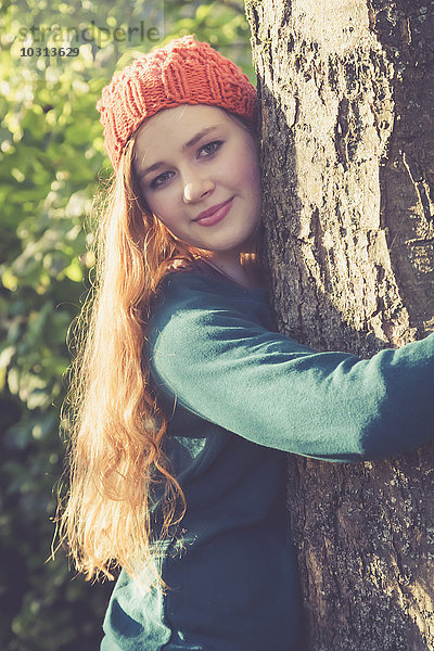 Porträt eines lächelnden Teenagermädchens beim Umarmen eines Baumes