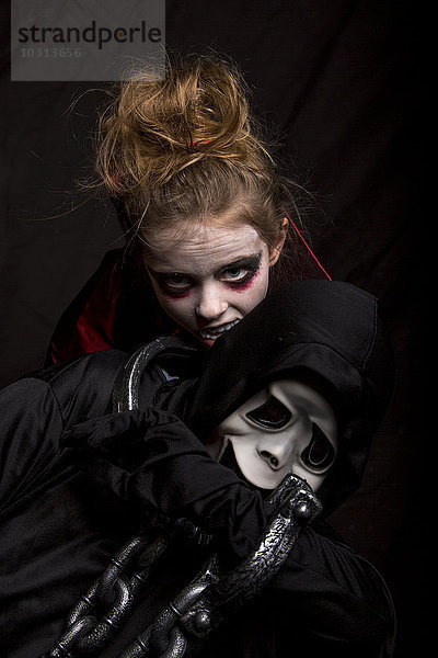 Mädchenmaske als Vampir beißender Junge mit Scream-Maske