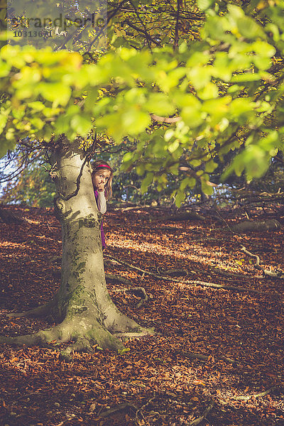 Kleines Mädchen  das sich hinter einem Baum im Wald versteckt.