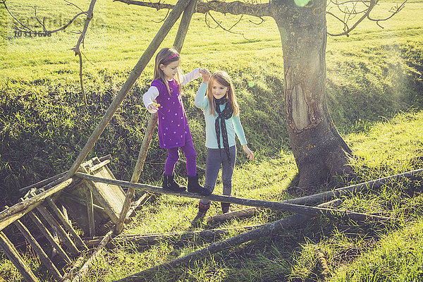 Mädchen hilft anderen kleinen Mädchen beim Balancieren auf einer Holzstange