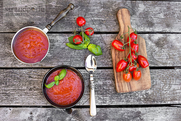 Topf und Schüssel mit hausgemachter Tomatensuppe auf Holz