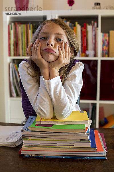 Porträt eines unglücklichen Mädchens  das sich auf einen Stapel Schulbücher stützt.