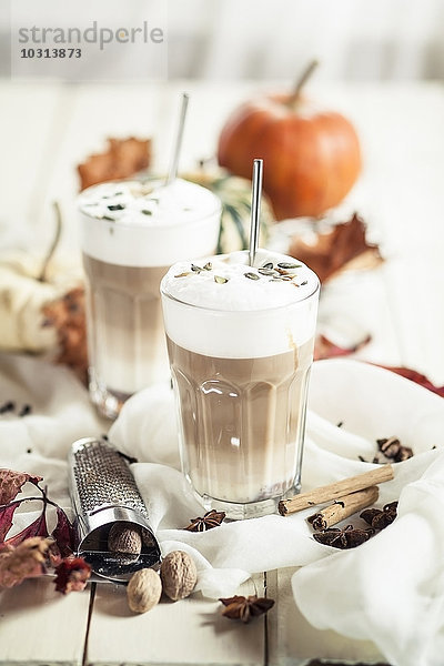 Zwei Gläser Kürbisgewürz Latte Macchiato zwischen Gewürzen und Herbstdekoration