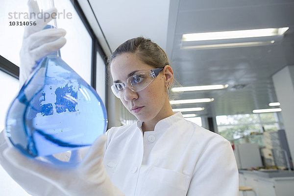 Junge Wissenschaftlerin mit Glaskolben in einem Chemielabor