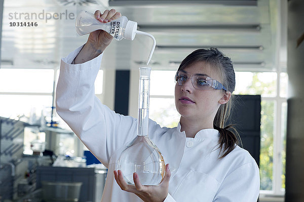 Junge Chemikerin beim Abfüllen von Wasser in einen Destillierkolben in einem chemischen Labor
