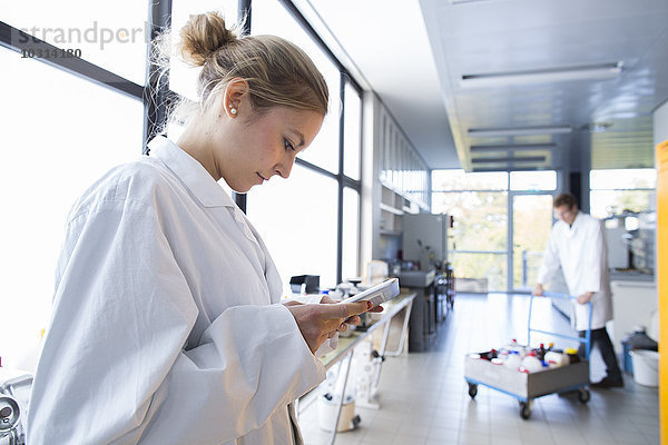 Junge Chemikerin mit digitaler Tablette im Chemielabor