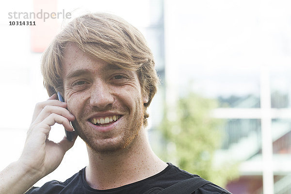 Porträt eines lächelnden jungen Mannes beim Telefonieren mit dem Smartphone