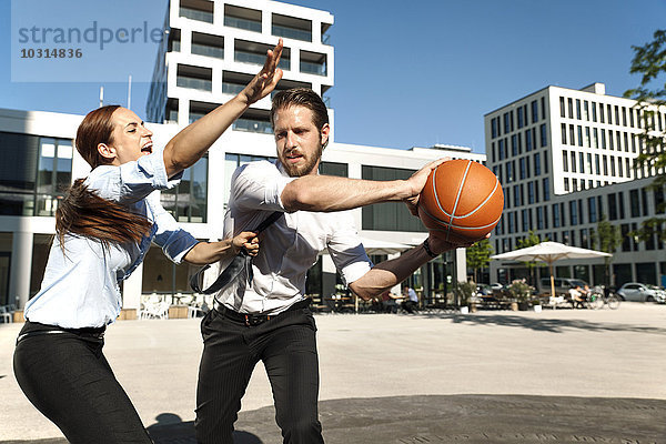 Geschäftsmann und Geschäftsfrau beim Basketballspielen im Freien