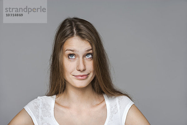 Porträt einer lächelnden jungen Frau vor grauem Hintergrund mit Blick nach oben