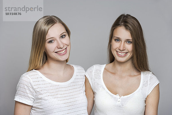 Porträt zweier lächelnder junger Frauen vor grauem Hintergrund