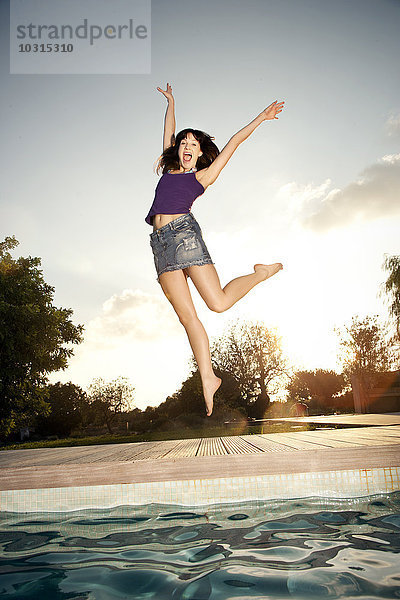 Überschwängliche junge Frau beim Springen am Pool