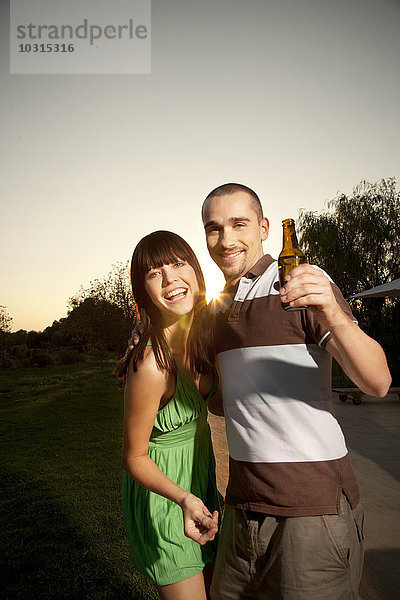 Glückliches junges Paar mit Bierflasche bei Sonnenuntergang