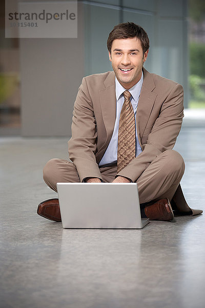 Lächelnder Geschäftsmann auf dem Boden sitzend mit Laptop