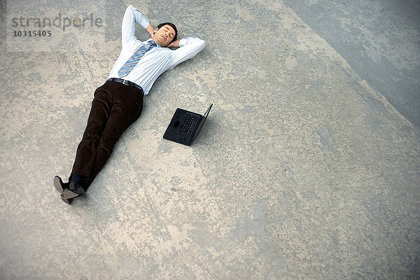 Geschäftsmann auf dem Boden neben dem Laptop liegend