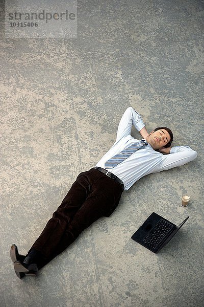 Geschäftsmann auf dem Boden neben dem Laptop liegend