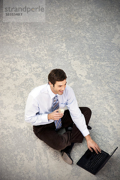 Lächelnder Geschäftsmann auf dem Boden sitzend mit Laptop