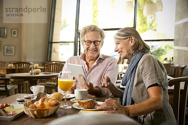 Lächelndes Seniorenpaar mit digitalem Tablett beim Frühstück im Café