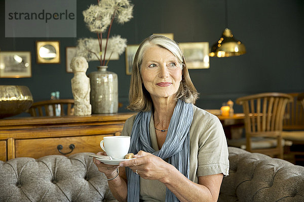 Lächelnde Seniorin im Aufenthaltsraum bei einer Tasse Kaffee