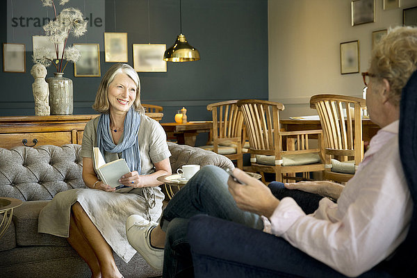 Lächelnde Seniorin auf der Couch im Aufenthaltsraum mit Blick auf den Ehemann