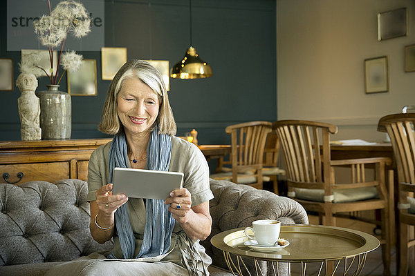 Lächelnde Seniorin im Aufenthaltsraum mit digitalem Tablett