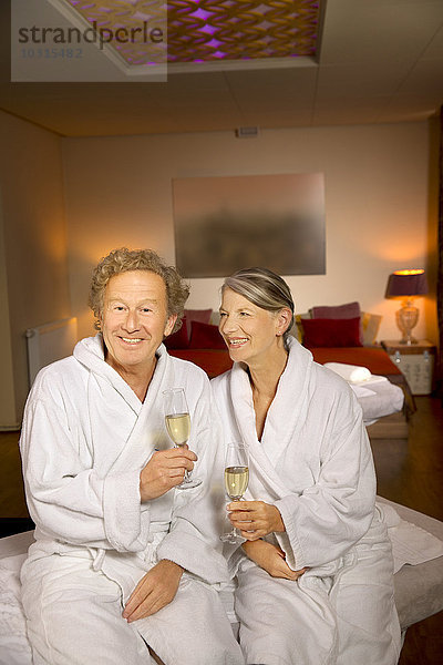 Lächelndes Seniorenpaar im Bademantel mit Sektgläsern