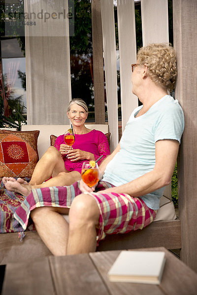 Lächelndes Seniorenpaar sitzt auf der Lounge im Freien mit Cocktails