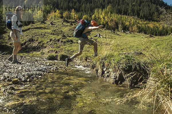 Österreich  Tirol  Tannheimer Tal  zwei junge Wanderer beim Überqueren des Wassers