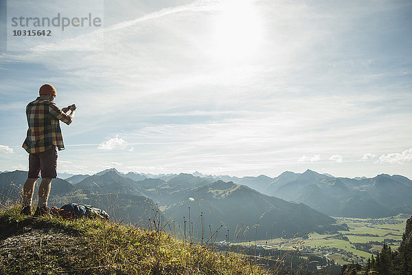 Österreich  Tirol  Tannheimer Tal  junger Mann beim Fotografieren in der Bergwelt