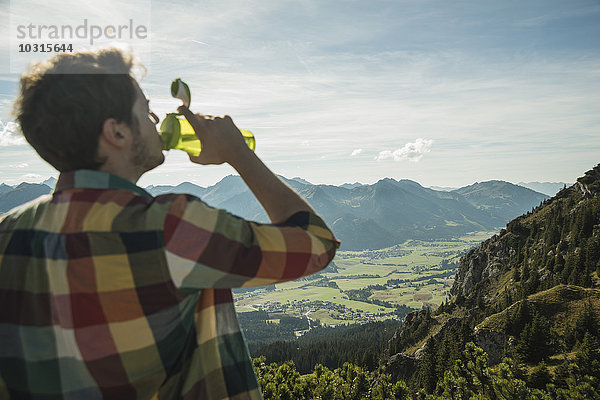 Österreich  Tirol  Tannheimer Tal  junger Mann trinkt Wasser in der Bergwelt