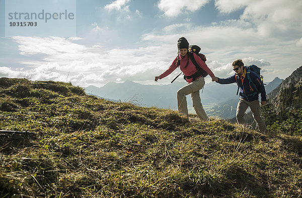 Österreich  Tirol  Tannheimer Tal  junges Paar wandert Hand in Hand auf der Alm