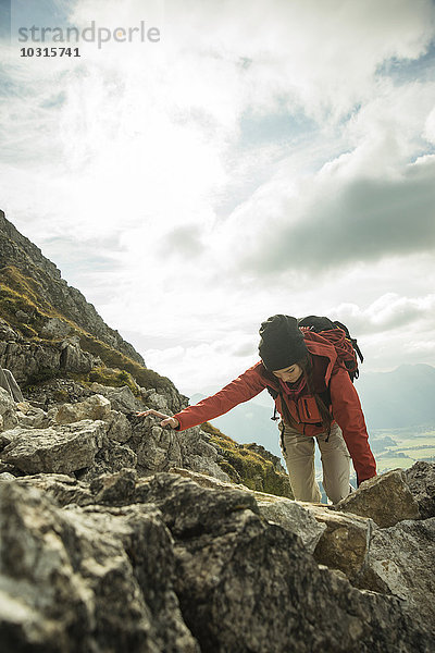 Österreich  Tirol  Tannheimer Tal  junge Frau klettert auf Felsen