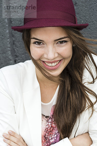 Porträt einer jungen lächelnden Frau mit langem braunem Haar und Hut