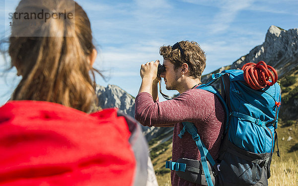 Österreich  Tirol  Tannheimer Tal  junger Mann auf Wanderung mit Blick durchs Fernglas