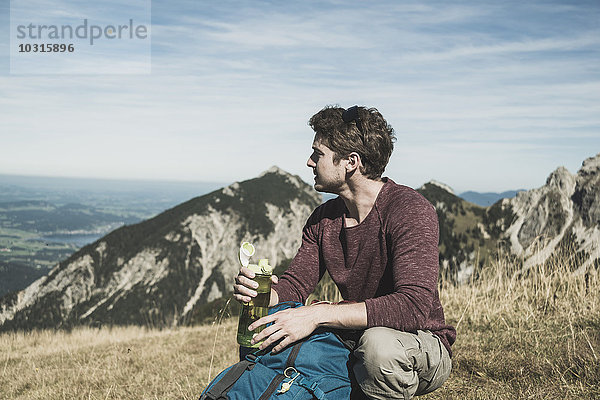 Österreich  Tirol  Tannheimer Tal  junger Mann mit Rucksack und Trinkflasche auf Almwiese