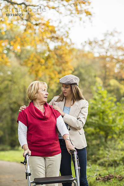 Seniorin und ihre fürsorgliche erwachsene Enkelin beim gemeinsamen Spaziergang im Herbstpark